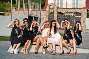 bachelorette party NYC: Group of 7 girls wear on black and 2 brides sitting on bench and having fun at hen party.