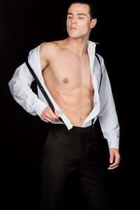 best male strippers in New York: muscular and confident man touching suspenders isolated on black