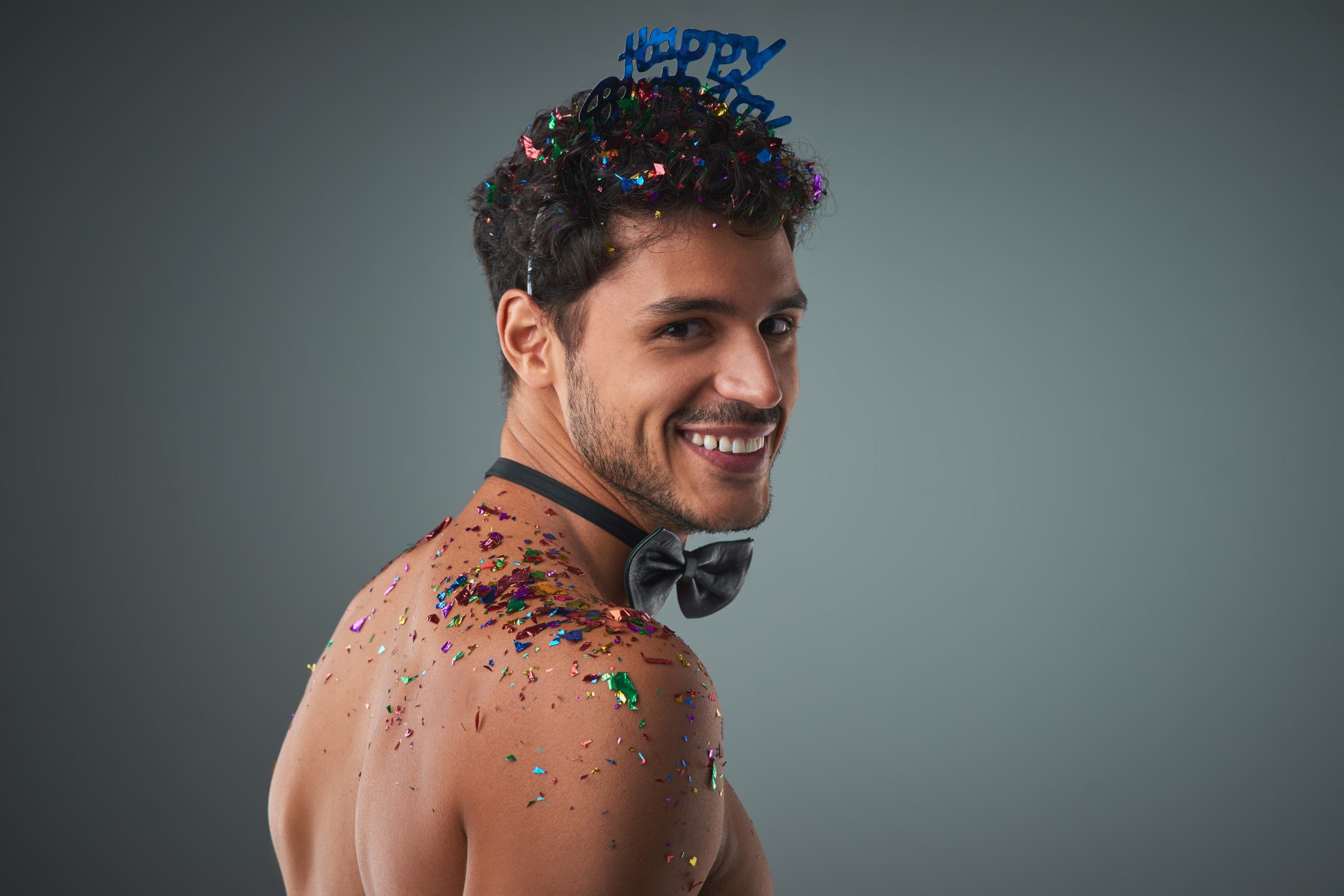 Studio shot of a handsome young shirtless man posing against a grey background.